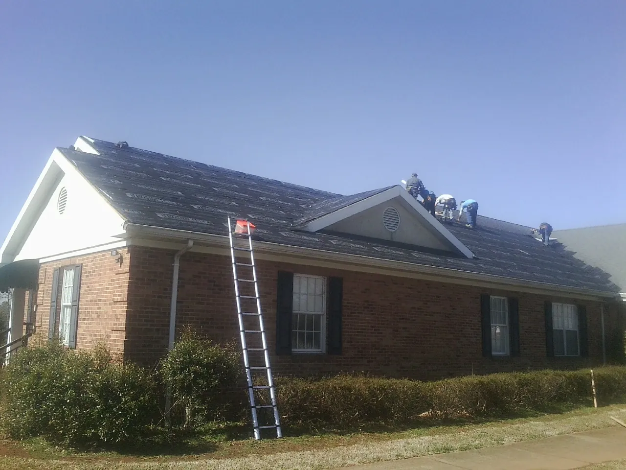 Crew tearing shingles off a brick ranch roof with a ladder set — Emergency Roof Repair work by our crew in Lemon Grove